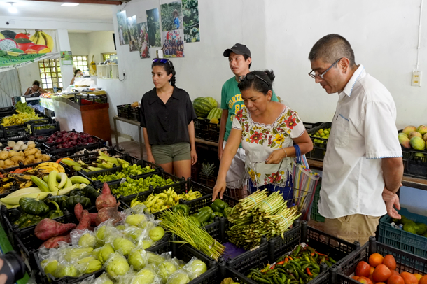 Ana Piña y vistantes comprando fruta en un mercado local